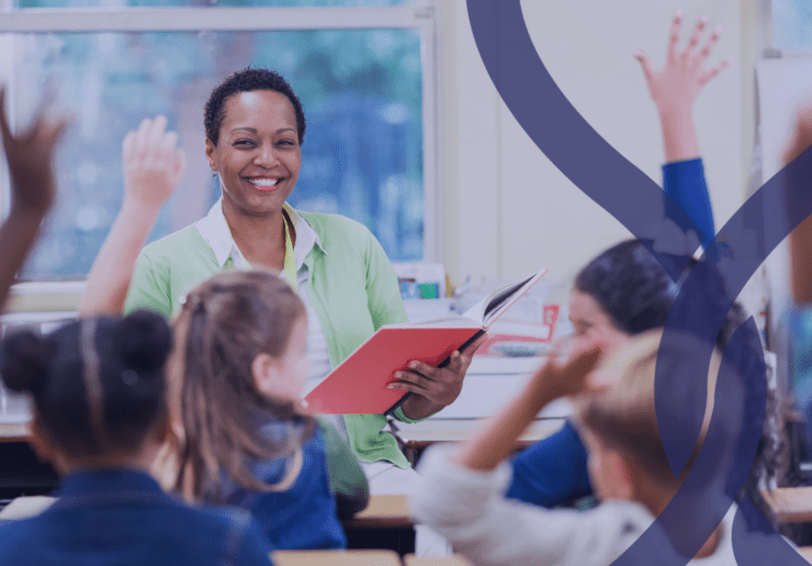 Teacher in a classroom with children sat at desks with their hands in the air