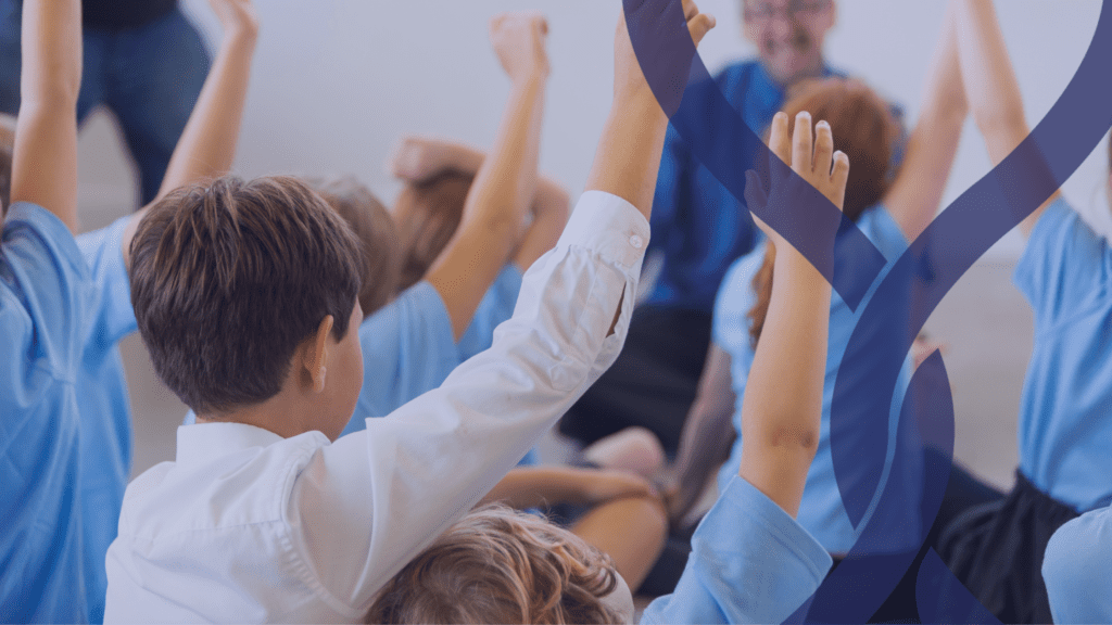 Group of primary school children sat on a carpet with their hands in the air
