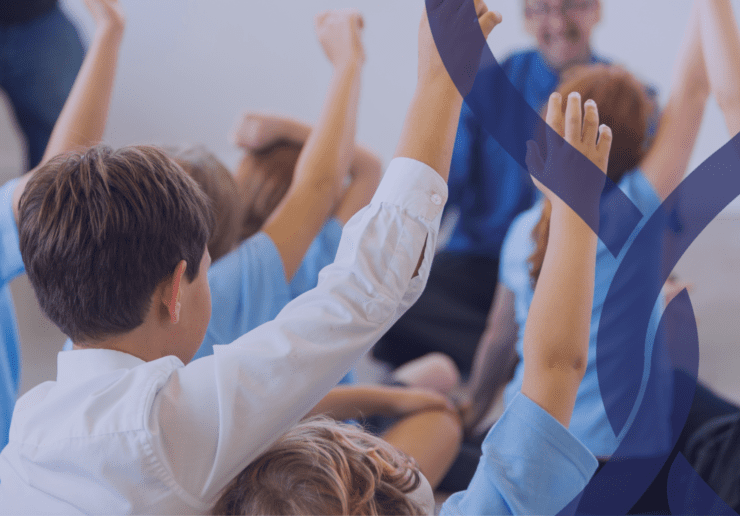 Group of primary school children sat on a carpet with their hands in the air